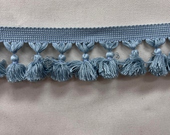 May include: A close-up of a light blue tassel trim with a woven base. The tassels are soft and fluffy, and the trim is perfect for adding a touch of elegance to any project.