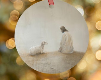 Può includere: Un ornamento rotondo in metallo bianco con un dipinto di un uomo inginocchiato e un agnello bianco che lo guarda. L'uomo indossa una tunica bianca e ha la barba. Lo sfondo è grigio chiaro.