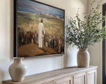Könnte beinhalten: Ein gerahmtes Gemälde zeigt eine Figur in weißen Gewändern, die über eine Menschenmenge blickt. Das Kunstwerk mit schwarzem Rahmen hängt über einem Holzschrank. Zwei dekorative Vasen und Grünzeug vervollständigen die Szene und schaffen ein ruhiges, künstlerisches Interieur.