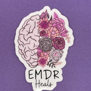May include: A white sticker with a pink and purple floral design on a brain outline. The text "EMDR Heals" is below the brain.