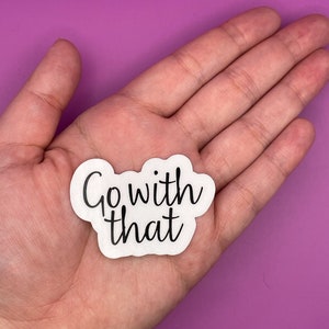 May include: White sticker with black text that reads "Go with that" on a pink background.