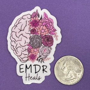 May include: A white sticker with a pink and purple floral design on a brain outline. The text "EMDR Heals" is below the design.