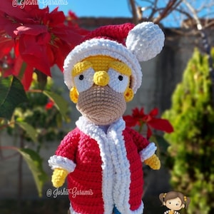 May include: A crocheted Santa Claus doll with yellow hair, a red and white suit, and a white hat. The doll is holding a red bag with a white trim. The doll is standing on a hand.