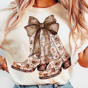 Puede incluir: Una camiseta blanca con un estampado floral marr&oacute;n y blanco de botas de vaquero atadas con un gran lazo marr&oacute;n.