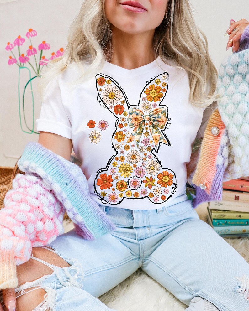 Puede incluir: Una camiseta blanca con un dise&ntilde;o de conejo floral. El conejo est&aacute; hecho de peque&ntilde;as flores en tonos naranja, amarillo, rosa y blanco. El conejo tiene un lazo hecho del mismo tejido floral.