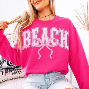Pu&ograve; includere: Una felpa rosa con la parola "BEACH" in lettere bianche e un fiocco rosa al centro. La felpa &egrave; realizzata in un materiale morbido e confortevole ed &egrave; perfetta per un abbigliamento casual.