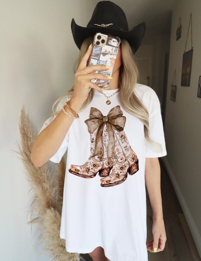 Puede incluir: Camiseta blanca con un estampado floral marr&oacute;n de botas de vaquero atadas con un lazo marr&oacute;n.