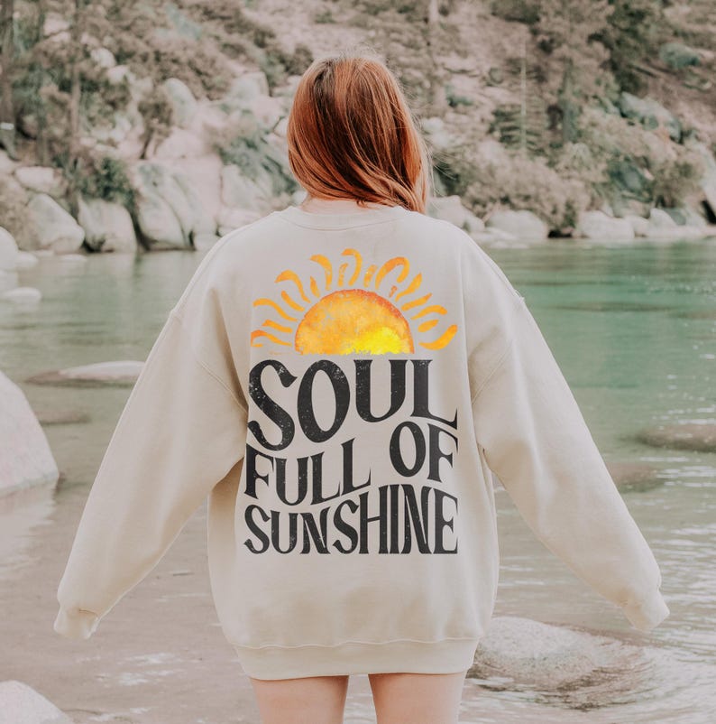 May include: A beige sweatshirt with a graphic of a yellow sun and the text "SOUL FULL OF SUNSHINE" printed on the back.