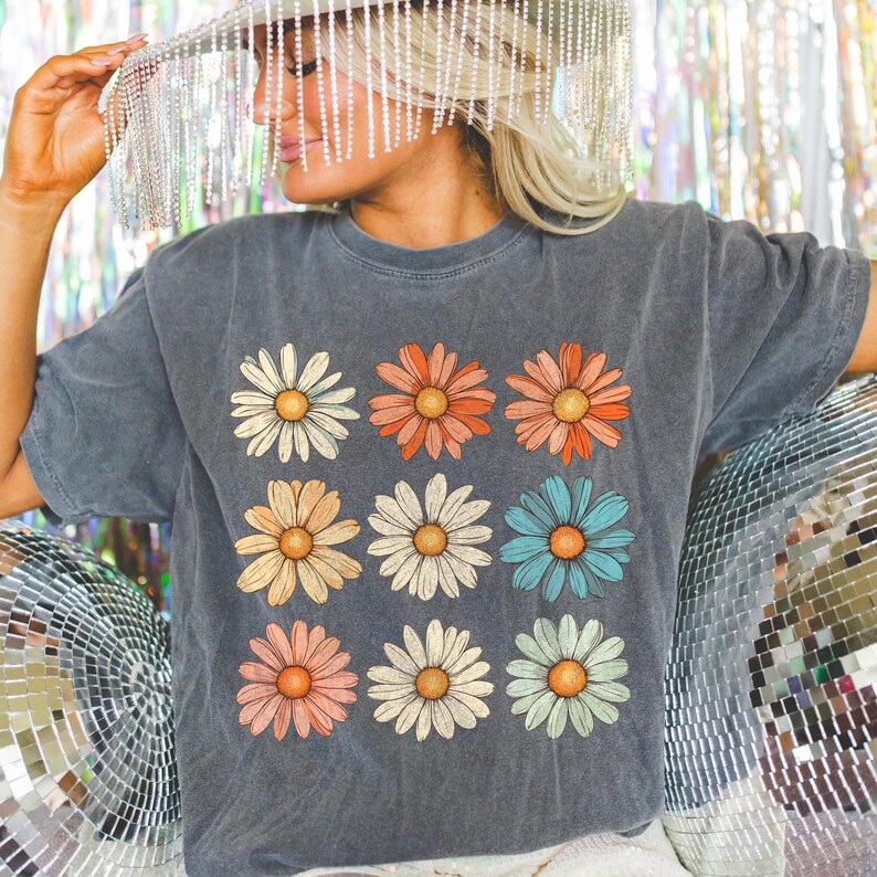 May include: A dark grey t-shirt with a vintage-inspired design featuring nine colourful daisies arranged in a grid pattern.