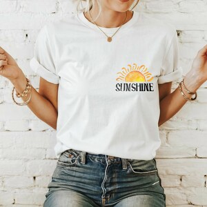May include: White t-shirt with a watercolor-style sun graphic and the word "SUNSHINE" printed in black.