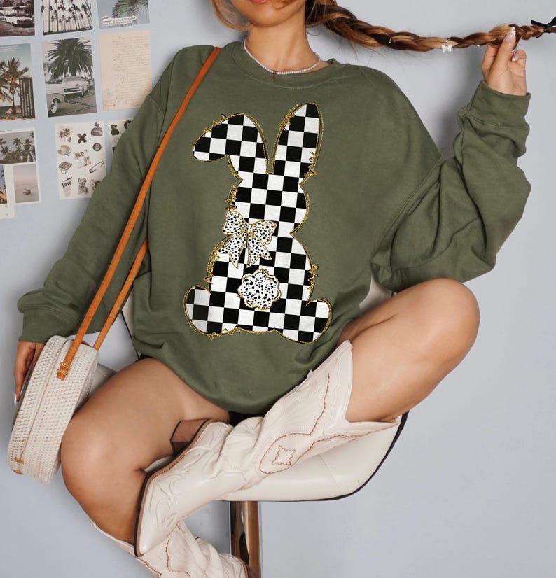 May include: A green sweatshirt with a checkered bunny graphic. The bunny has a gold bow and is outlined in gold. The sweatshirt has long sleeves and a crew neck.