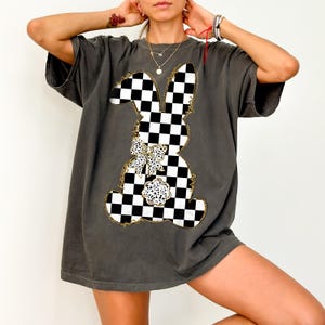 May include: A charcoal gray oversized t-shirt with a black and white checkered bunny graphic. The bunny has a large bow with white polka dots.