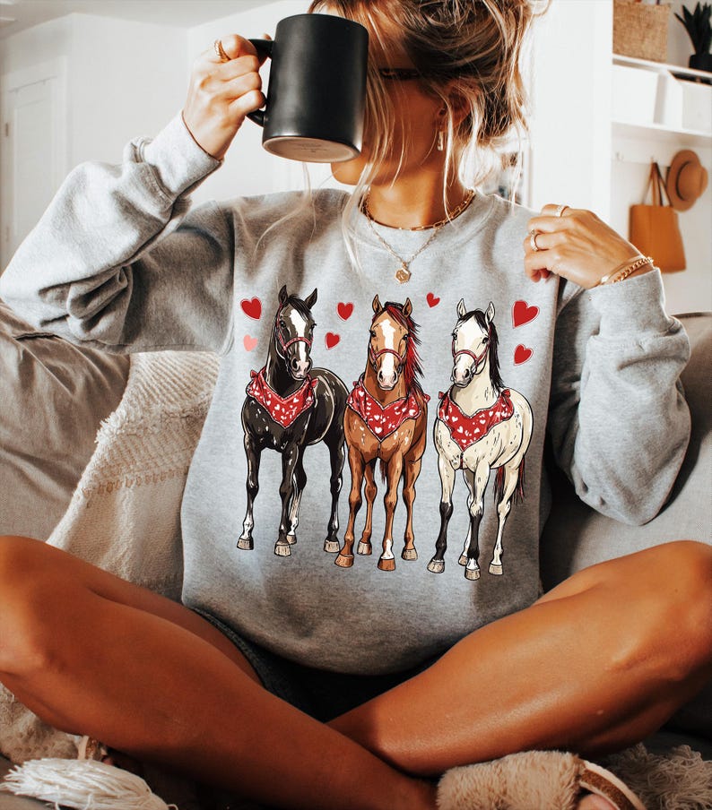 Puede incluir: Una sudadera gris con un gr&aacute;fico de tres caballos con bandanas y corazones. Los caballos son marr&oacute;n, blanco y negro.