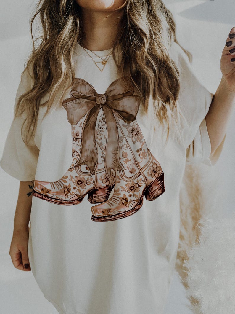 Puede incluir: Camiseta blanca con un estampado floral marr&oacute;n de botas de vaquero atadas con un gran lazo marr&oacute;n.