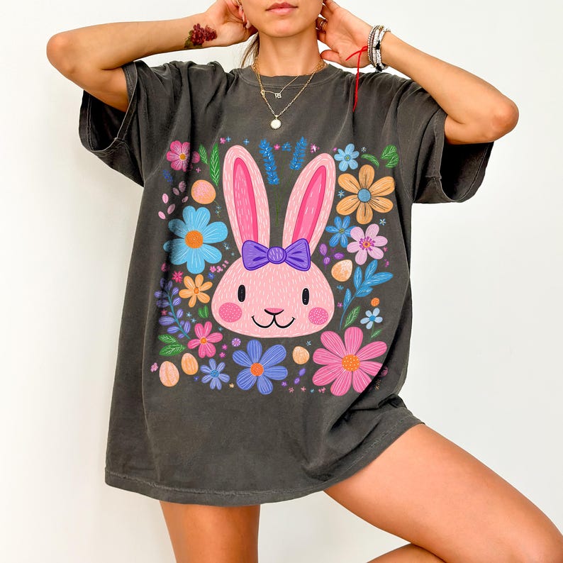 May include: A dark gray oversized t-shirt with a pink bunny rabbit wearing a purple bow surrounded by colorful flowers. The bunny is the center of the graphic design on the shirt.