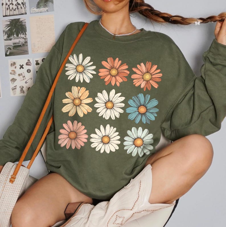 May include: A green long-sleeved sweatshirt with a crew neck and a pattern of nine colourful daisies.