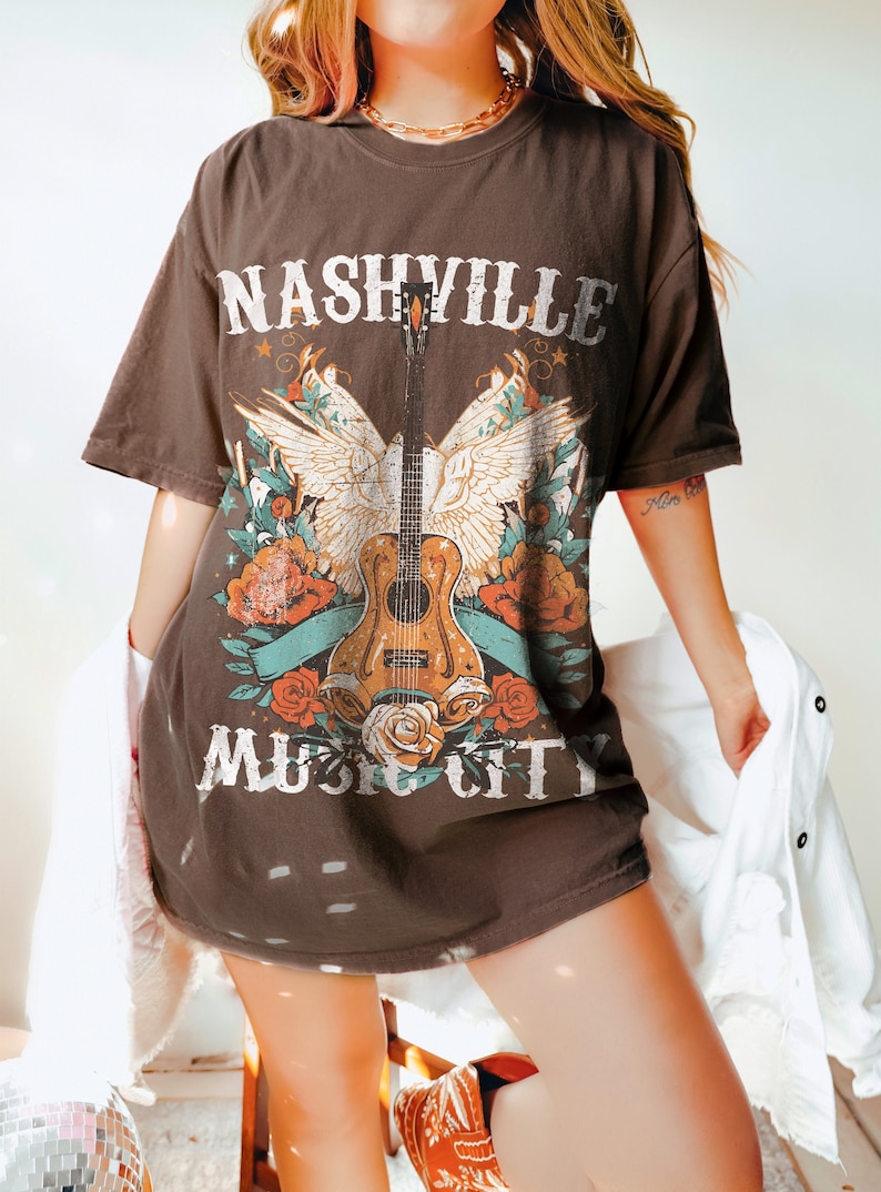 May include: A brown t-shirt with a graphic print of a guitar with wings, flowers, and the text "Nashville Music City".
