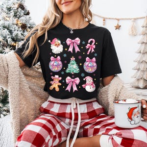 May include: A black t-shirt with a Christmas-themed design featuring Santa, a gingerbread person, a snowman, ornaments, bows, and candy canes.