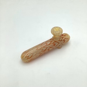 May include: A small, clear glass pipe with a red and white geometric pattern. The pipe has a bowl on one end and a mouthpiece on the other.