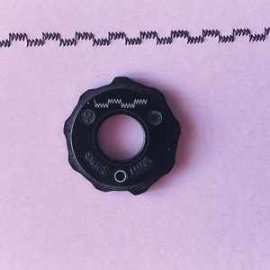 May include: A black sewing machine foot with the text "Swiss Made" and "13" printed on it.