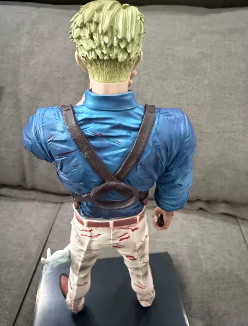 May include: A figurine of a character with light green hair, wearing a blue shirt, brown suspenders, and white pants with red accents. The figure is holding a white object and is standing on a dark base.