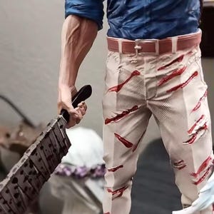 May include: A detailed figurine of a character in a blue shirt, tan pants with red slashes, and a yellow tie. The figure holds a large, blood-splattered cleaver. The figurine's belt is brown, and the pants have a distressed look.
