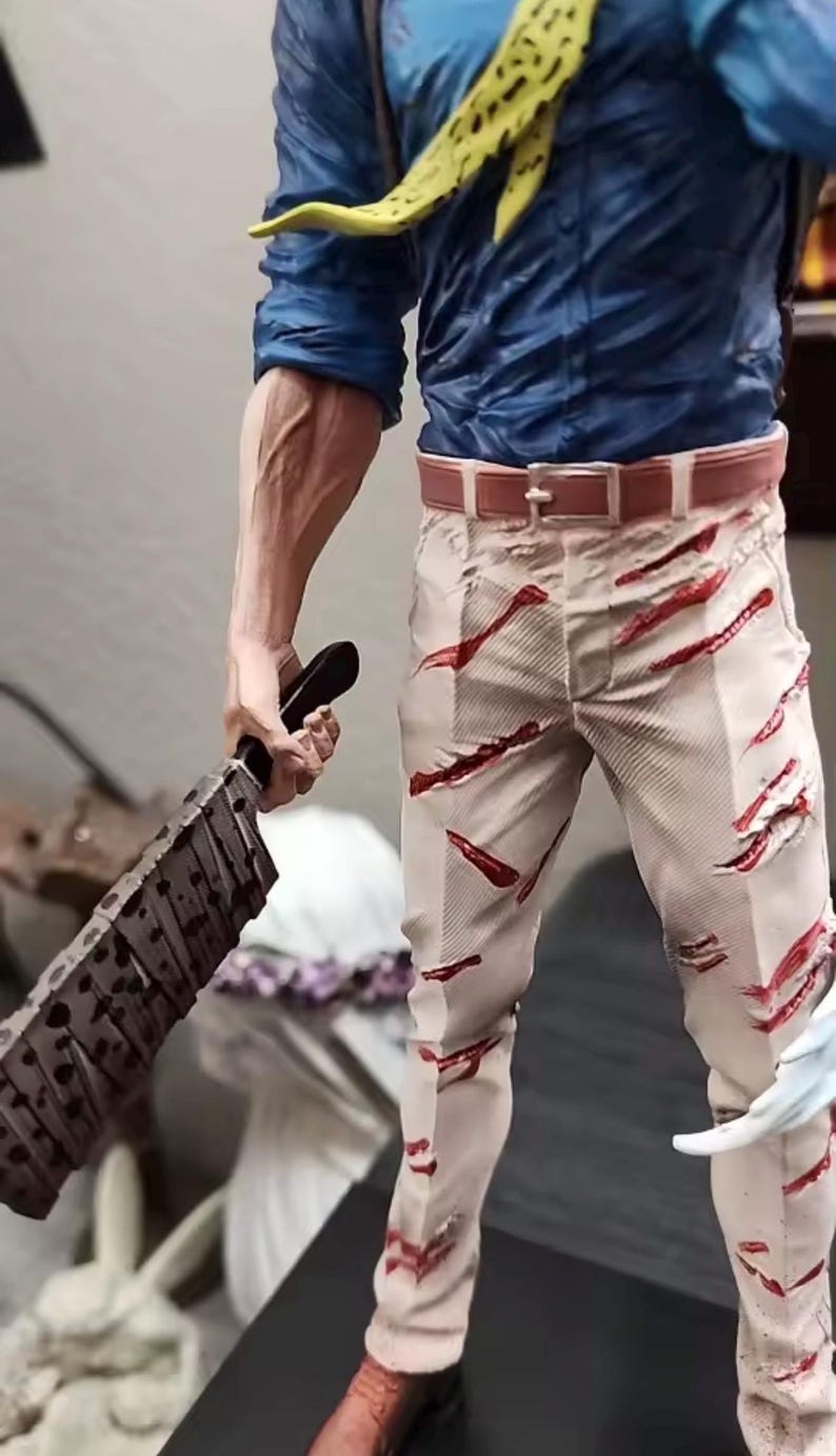 May include: A detailed figurine of a character in a blue shirt, tan pants with red slashes, and a yellow tie. The figure holds a large, blood-splattered cleaver. The figurine's belt is brown, and the pants have a distressed look.