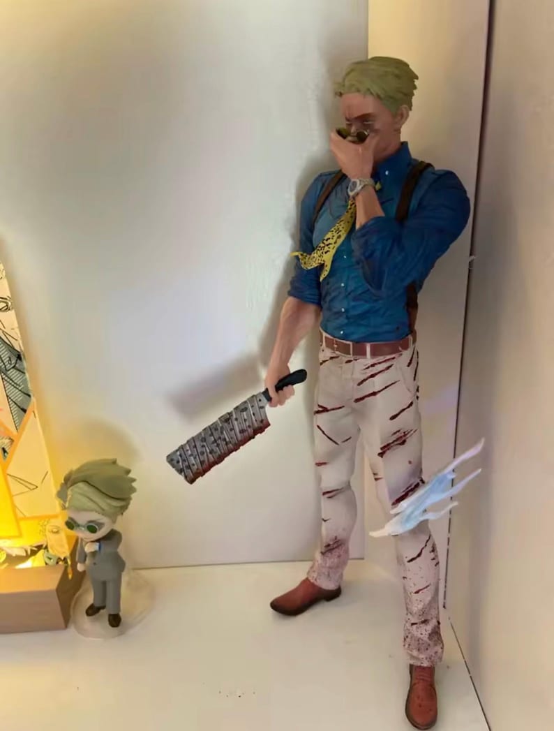 May include: A detailed figurine of a character from an anime series, wearing a blue shirt, suspenders, and white pants with red streaks. The character holds a large cleaver and has a yellow patterned tie. A smaller figurine is also present.