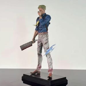 May include: A detailed figurine of a character in a blue shirt, gray pants, and brown boots, holding a large cleaver. The figure has green hair and a yellow tie. A blue energy effect is near the figure's feet. The figure is on a black base.