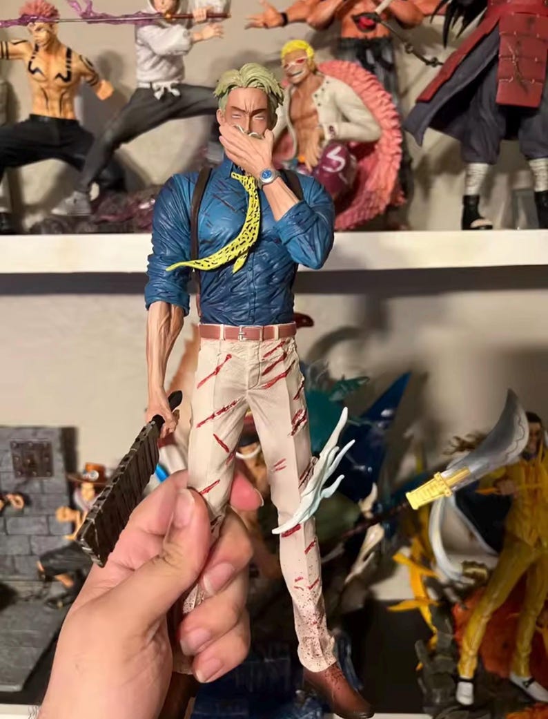 May include: A detailed figurine of a character in a blue shirt, tan pants with red streaks, and a yellow patterned tie. The figure is holding a weapon and has a watch on its wrist. Other figurines are visible on a shelf in the background.