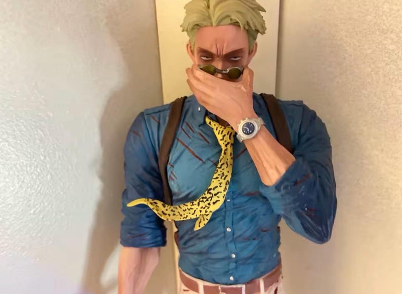 May include: A figurine of a character wearing a blue shirt, brown suspenders, and a yellow patterned tie. The character is wearing sunglasses and a silver watch. The figurine is a collectible item.
