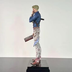 May include: A detailed figurine of a character in a blue shirt, light gray pants, and brown boots. The figure is holding a large, dark brown object with red accents. The figure is standing on a black base.