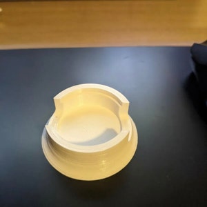 Puede incluir: Base circular de pl&aacute;stico blanco impresa en 3D con una parte superior circular y un borde elevado.