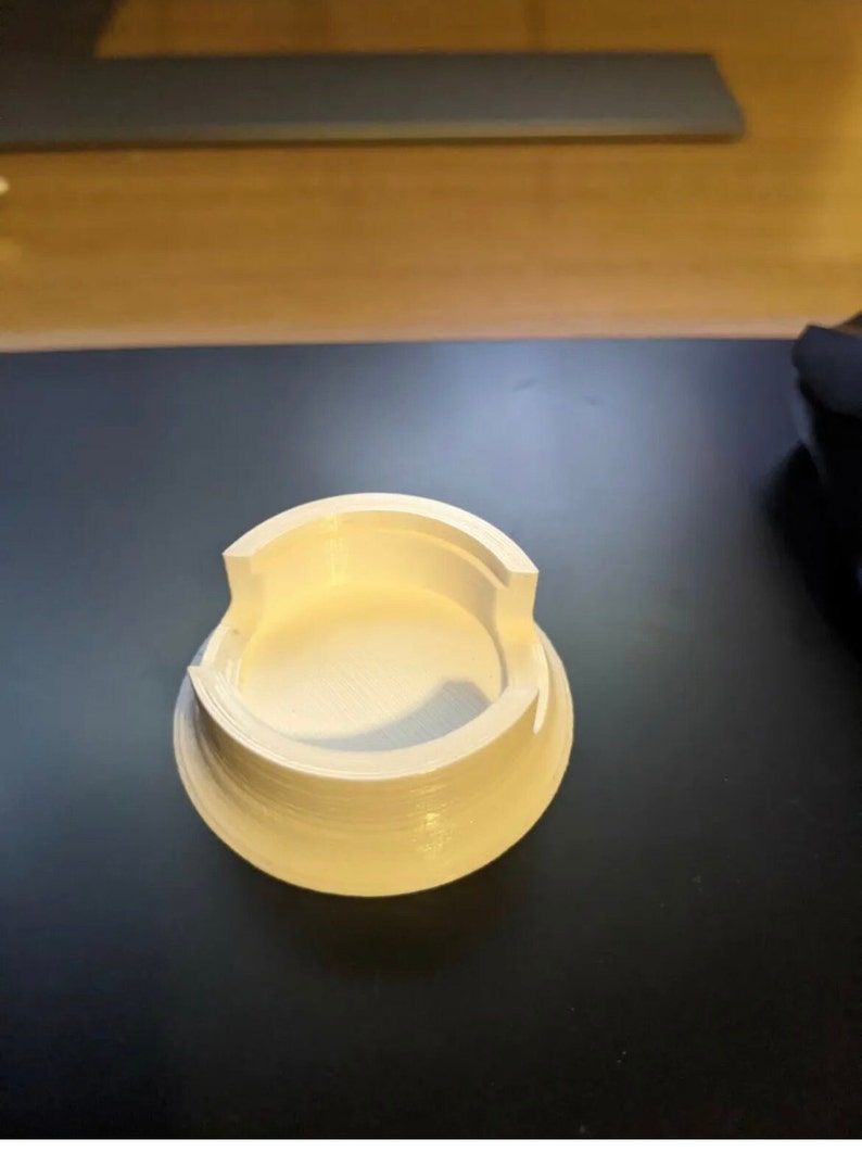 Puede incluir: Base circular de pl&aacute;stico blanco impresa en 3D con una parte superior circular y un borde elevado.