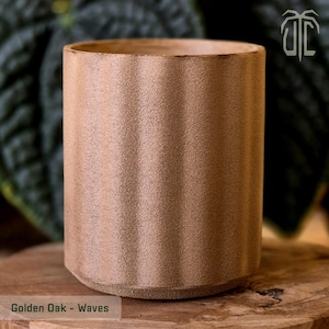Peut inclure: Un récipient cylindrique en bois de chêne doré, avec une surface texturée et des motifs ondulés verticaux. Le récipient a une base évasée. Le texte "Golden Oak - Waves" est en bas. Idéal pour la décoration intérieure.