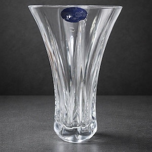Könnte beinhalten: Transparente Kristallvase mit ausgestellter Oberseite und strukturiertem, vertikalem Design. Die Vase hat einen facettierten Boden und ein blaues Etikett in der Nähe der Oberseite. Ein dekoratives Stück für das Zuhause.