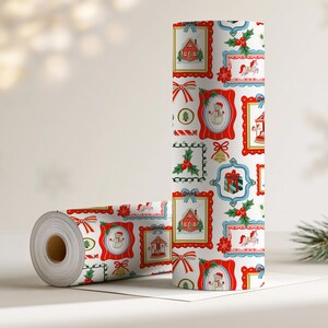Pu&ograve; includere: Un rotolo di carta da regalo bianca con un motivo natalizio ripetuto di cornici ornate rosse e blu contenenti illustrazioni di case, pupazzi di neve, cavalli da giostra e regali, arricchito da foglie di agrifoglio e fiocchi rossi.