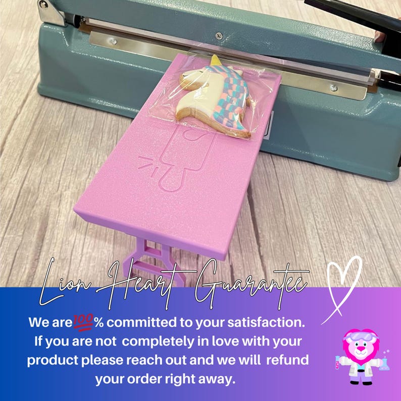 Puede incluir: Una mesa rosa con una galleta de unicornio encima. La mesa se est&aacute; sellando en una bolsa de pl&aacute;stico con una selladora t&eacute;rmica. El texto "Lion Heart Guarantee" es visible en la imagen. El texto "We are 100% committed to your satisfaction. If you are not completely in love with your product please reach out and we will refund your order right away." tambi&eacute;n es visible en la imagen.