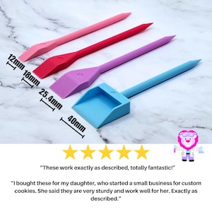 May include: Four plastic tools for decorating cookies. The tools are pink, red, purple, and blue. The tools are different sizes, with the smallest being 1.2 inches long and the largest being 1.6 inches long. The tools are on a white marble surface.