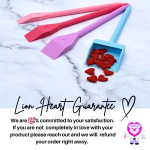 May include: Three pink and blue plastic spatulas with heart-shaped handles, a blue plastic dustpan with a heart-shaped handle, and red heart-shaped sprinkles. The text "Lion Heart Guarantee" is written in black on a white background. A cartoon lion wearing a lab coat and glasses is in the bottom right corner.