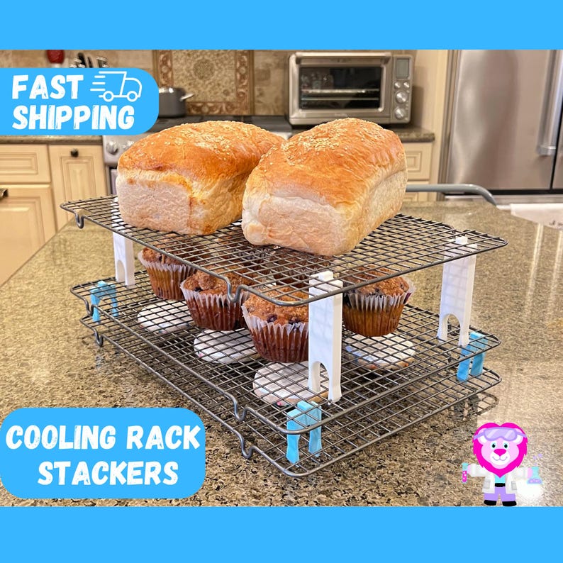K&ouml;nnte beinhalten: Zwei silberne K&uuml;hlroste, die &uuml;bereinander gestapelt sind und mit wei&szlig;en Clips zusammengehalten werden. Auf dem oberen Rost liegen zwei Wei&szlig;brote. Auf dem unteren Rost liegen sechs Muffins. Die Roste stehen auf einer grauen Arbeitsplatte.