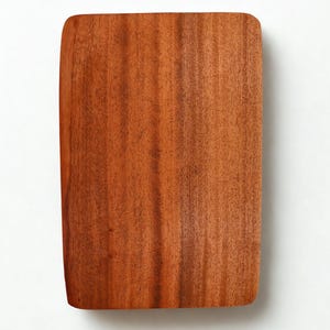 May include: A rectangular wooden cutting board with rounded corners. The board has a reddish-brown color and a visible wood grain pattern. The cutting board is made of a solid piece of wood.