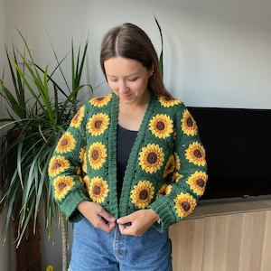 May include: A green crocheted cardigan with a sunflower pattern. The cardigan is cropped and has a button closure.
