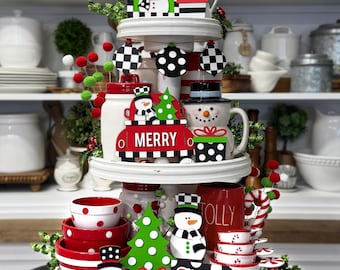 May include: A tiered tray decorated for Christmas with a snowman theme. The tray features red and white polka dot ornaments, a snowman mug, a snowman figurine, a green and white Christmas tree, and a sign that says "Merry & Bright".