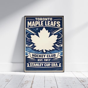 Puede incluir: Un póster enmarcado con el logotipo de los Toronto Maple Leafs. El diseño presenta una gran hoja de arce blanca sobre un fondo azul, con el texto "Toronto Maple Leafs Hockey Club Est. 1917 Stanley Cup Era".