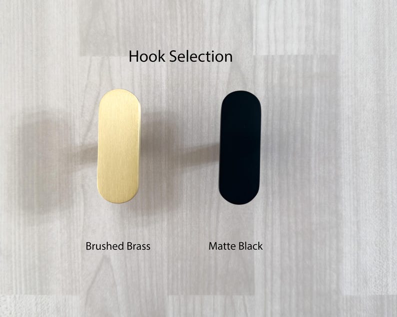 May include: Image of two modern hooks: one brushed brass and one matte black. The hooks are oval-shaped with a flat front and rounded top and bottom. The text "Hook Selection" is above the hooks.
