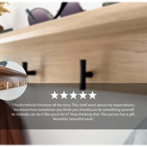 May include: A wooden shelf with black and gold hooks. The shelf is made of light-colored wood and has a dark wood section with gold hooks. The shelf is mounted on a wall and has a minimalist design.
