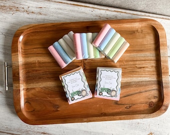 May include: A wooden serving tray holds pastel-colored chalk sticks and two small gift boxes. The gift boxes have a tractor illustration and text that reads "Thank you for celebrating with me!" The chalk is in shades of pink, blue, and green.