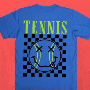 May include: A royal blue t-shirt with a black and white checkered pattern and a green smiley face tennis ball graphic. The text "TENNIS" is printed in green above the graphic.