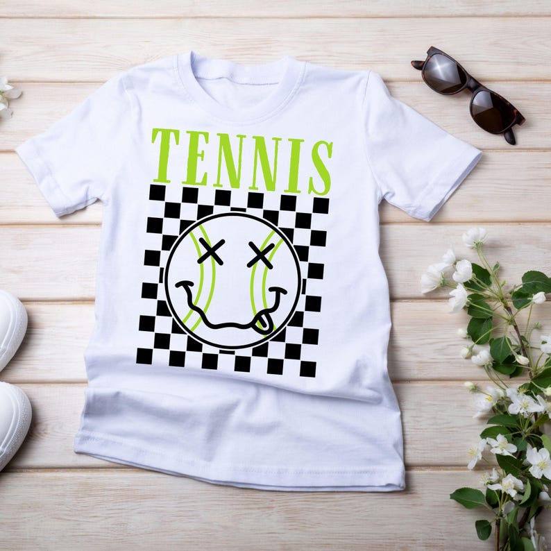 May include: White t-shirt with a black and white checkered pattern and a green tennis ball with a smiley face. The text "TENNIS" is printed in green above the ball.